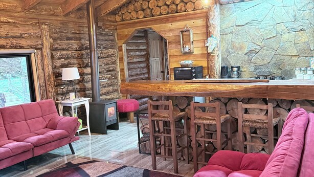 A cozy log cabin interior with a red sofa, a wooden bar area, and a stone wall. - Mountain cabin, natural environment, Huequecura river tourist attractions (Santa barbara)