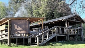 A rustic wooden cabin with a covered porch and a staircase leading to an upper level. - Mountain cabin, natural environment, Huequecura river tourist attractions (Santa barbara)