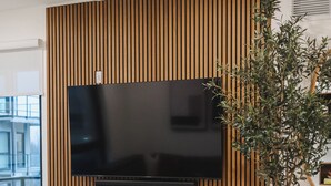 Ett modernt vardagsrum med en platt-TV som är monterad på en väggpanel av trä, en öppen spis nedanför och en krukväxt till höger.