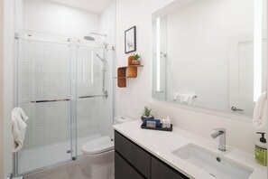 Ein modernes Badezimmer mit Duschkabine aus Glas, Toilette in Weiß, Waschtisch und Spiegel.