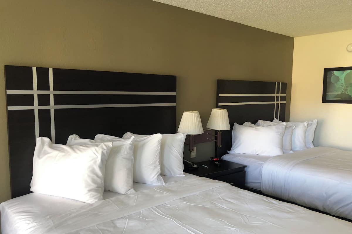 A hotel room with two beds, white bedding, and a nightstand with two lamps.