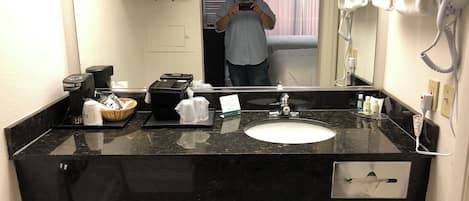 A hotel bathroom with a black marble sink, a mirror, a hairdryer, and a towel rack.