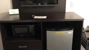 A dark wooden TV stand with a flat-screen TV, a microwave, and a refrigerator.