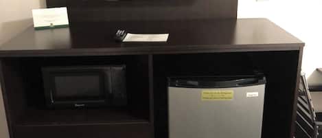 A dark wooden TV stand with a flat-screen TV, a microwave, and a refrigerator.