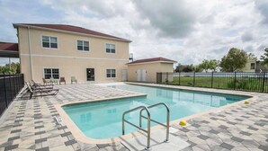 A swimming pool with a tiled deck, a metal ladder, and lounge chairs.