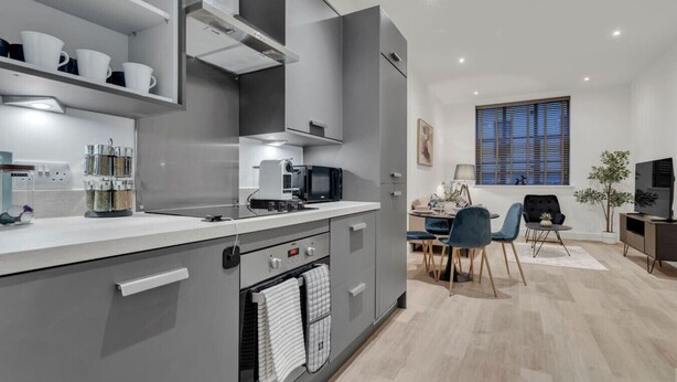 Une cuisine moderne avec des meubles de couleur grise, un four encastré et un coin repas comprenant une table et des chaises.