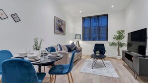 Un salon moderne comprenant un coin repas, un canapé, un téléviseur et une fenêtre avec des stores.