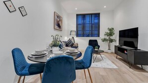 Un espace repas moderne avec une table ronde, des chaises bleues et un téléviseur posé sur un meuble noir.