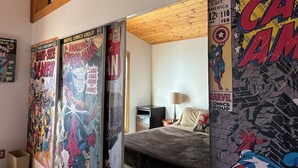 A room with a bed, a desk, and a wall covered with comic book posters.