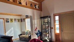 A living room with a high ceiling, a glass display cabinet, a door with a doormat, and a staircase.