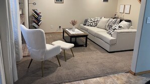 A living room with a white sofa, a white armchair, a coffee table, and a bookshelf. - Cozy Home in Beaverton (Aloha)