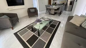 A modern living room with a sofa, armchair, and coffee table. A dining area with a table and chairs is visible in the background. - Lujoso con una habitación y vista al mar (Cabo San Lucas)