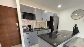 A modern kitchen with grey cabinets, a black microwave, a built-in oven, a refrigerator, and a sink. - Lujoso con una habitación y vista al mar (Cabo San Lucas)