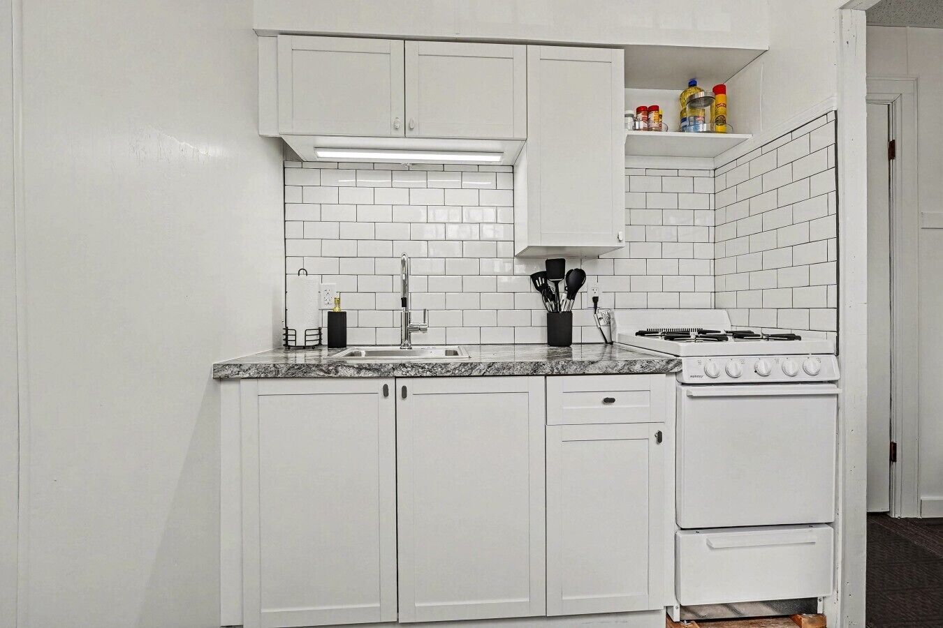 Una cocina con gabinetes blancos, encimera de granito, estufa y lavaplatos.