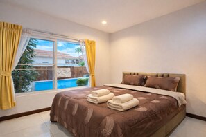 A bedroom with a bed, a window with curtains, and a view of a swimming pool. - Tropical Private Villa 2 (Pattaya City)