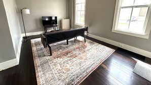 Un salon spacieux doté d’un parquet en bois foncé, d’un grand tapis à motifs, d’un canapé foncé, d’un lampadaire, d’une télévision et d’un ventilateur de plafond.
