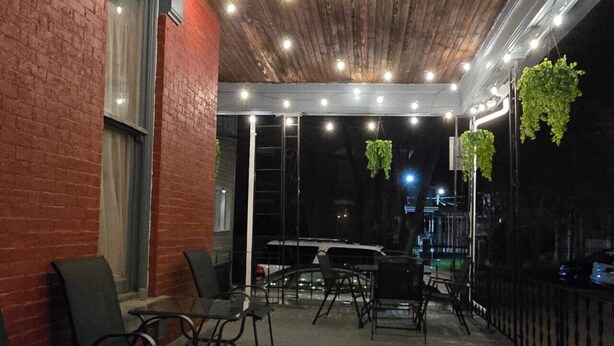 Un espace extérieur aménagé en patio, avec un plafond en bois, des plantes suspendues et des sièges d’extérieur.