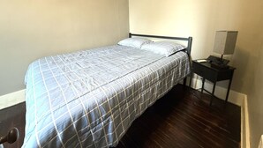 Un lit simple avec une couvre-lit matelassé, une table de chevet avec une lampe et un plancher en bois.