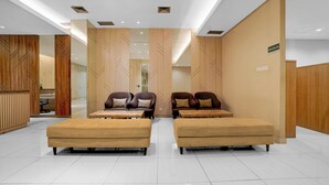 A modern lobby with two sofas and two armchairs, a reception desk, and a sign indicating the main entrance. - OYO 95052 Cordia Tower (Gunung Putri)