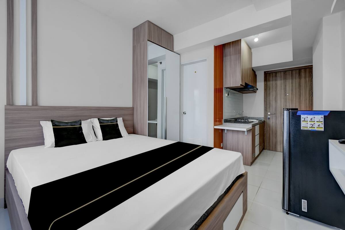 A hotel room with a bed, a small kitchenette, and a refrigerator.