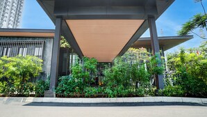 A modern building with a covered entrance, surrounded by greenery and a clear sky. - OYO 95052 Cordia Tower (Gunung Putri)