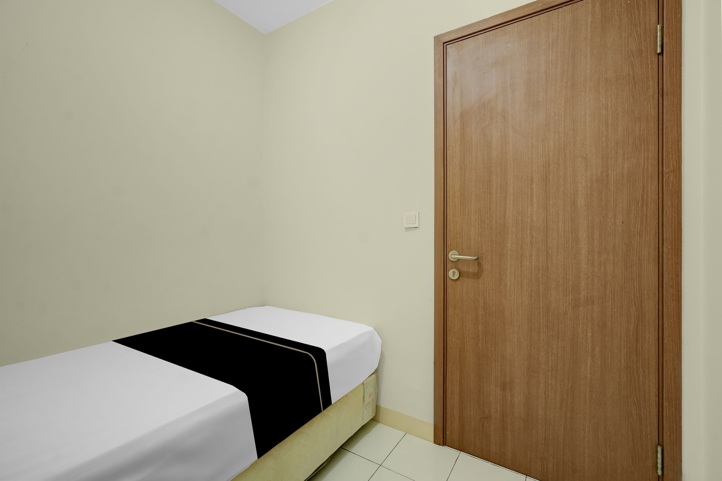 Una habitación pequeña con una cama individual, una puerta de madera y una pared de color claro.