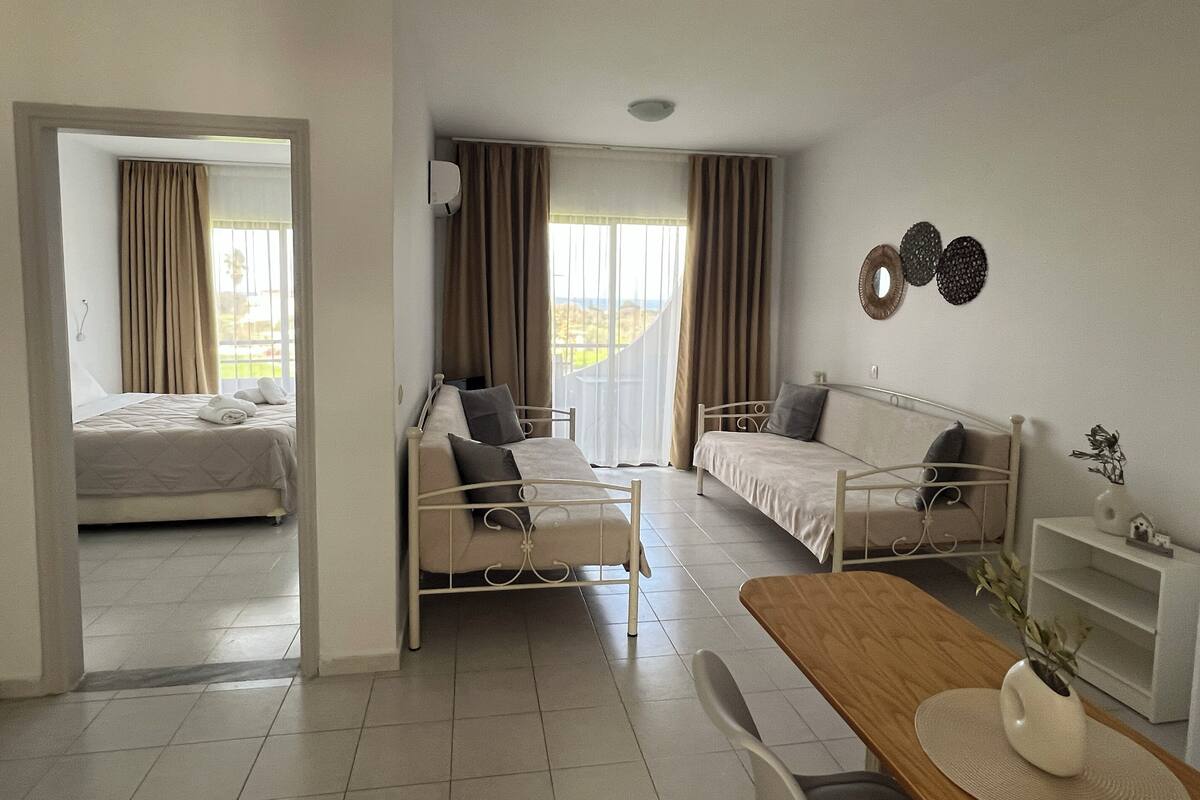 A hotel room with a bed, a sofa, a dining table, and a view of the outdoors.
