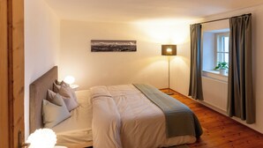 A bedroom with a bed, bedside table, lamp, and a view of the outdoors through a window. - Idyllic apartment on the Ritten - peace, nature & views of the Dolomites. Mobilcard incl (Trentino-Alto Adige)