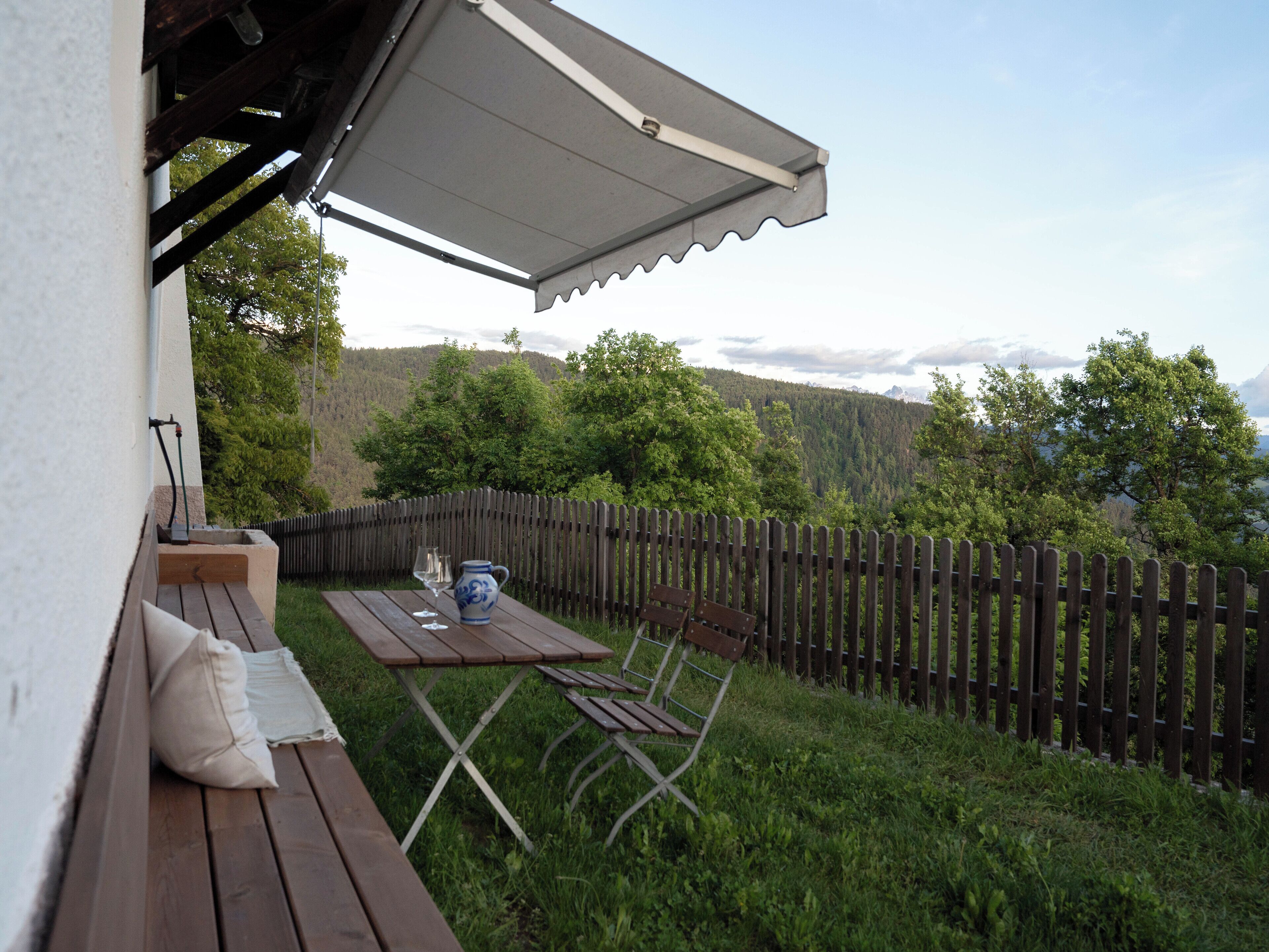 Un patio con una mesa y sillas, una valla de madera y vistas a un área boscosa.