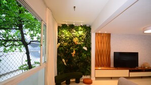 Un salon moderne doté d’une grande fenêtre, d’un mur végétal, d’un téléviseur à écran plat et d’un meuble en bois.