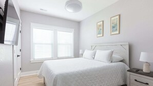 Une chambre avec un grand lit, une table de chevet avec une lampe et deux tableaux encadrés accrochés au mur.