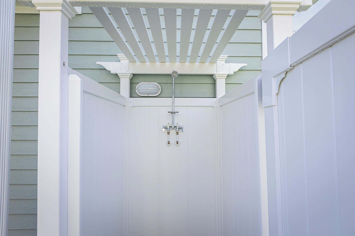 A white, enclosed outdoor shower area with a ceiling fan and a small window.