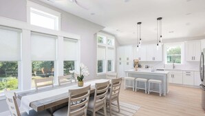 Una cocina moderna con armarios blancos, una isla central y una zona de comedor con mesa y sillas de madera.