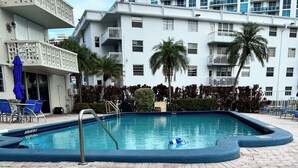 A swimming pool with a hexagonal tile floor, surrounded by a white building with balconies and palm trees. - Cozy 1-bedroom condo in peaceful Hallandale Beach with AC (Hallandale Beach)