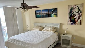 A bedroom with a bed, nightstands, a ceiling fan, a window with curtains, and artwork on the wall. - Cozy 1-bedroom condo in peaceful Hallandale Beach with AC (Hallandale Beach)