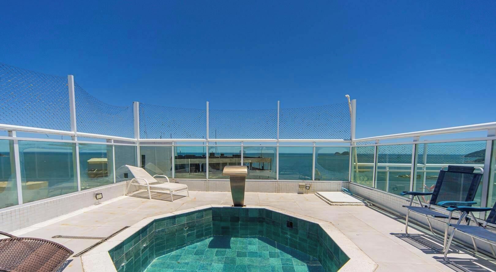 Un espace piscine aménagé sur le toit, avec un ciel bleu dégagé, un jacuzzi et des chaises longues.