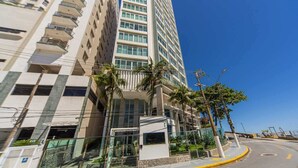 Un hotel moderno con facciata in vetro, diversi piani e una strada ad arco con palme.