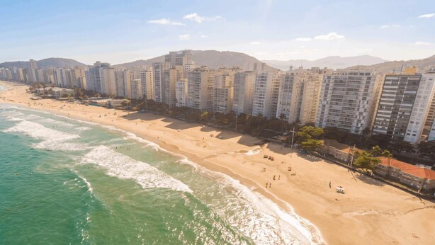 Paesaggio costiero urbano con grattacieli lungo la spiaggia, cieli sereni e mare calmo.
