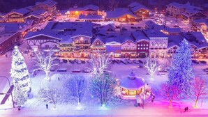Ein verschneites Dorf mit beleuchteten Gebäuden und Bäumen, das eine winterliche Stimmung vermittelt.