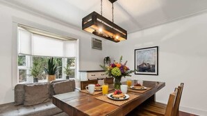 Un comedor con una mesa de madera, sillas y un banco. Hay un jarrón con flores sobre la mesa, y un cuadro en la pared.