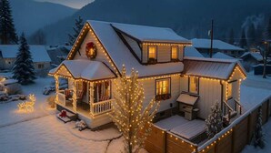 Una casa cubierta de nieve con un porche y terraza, iluminada por luces colgantes.
