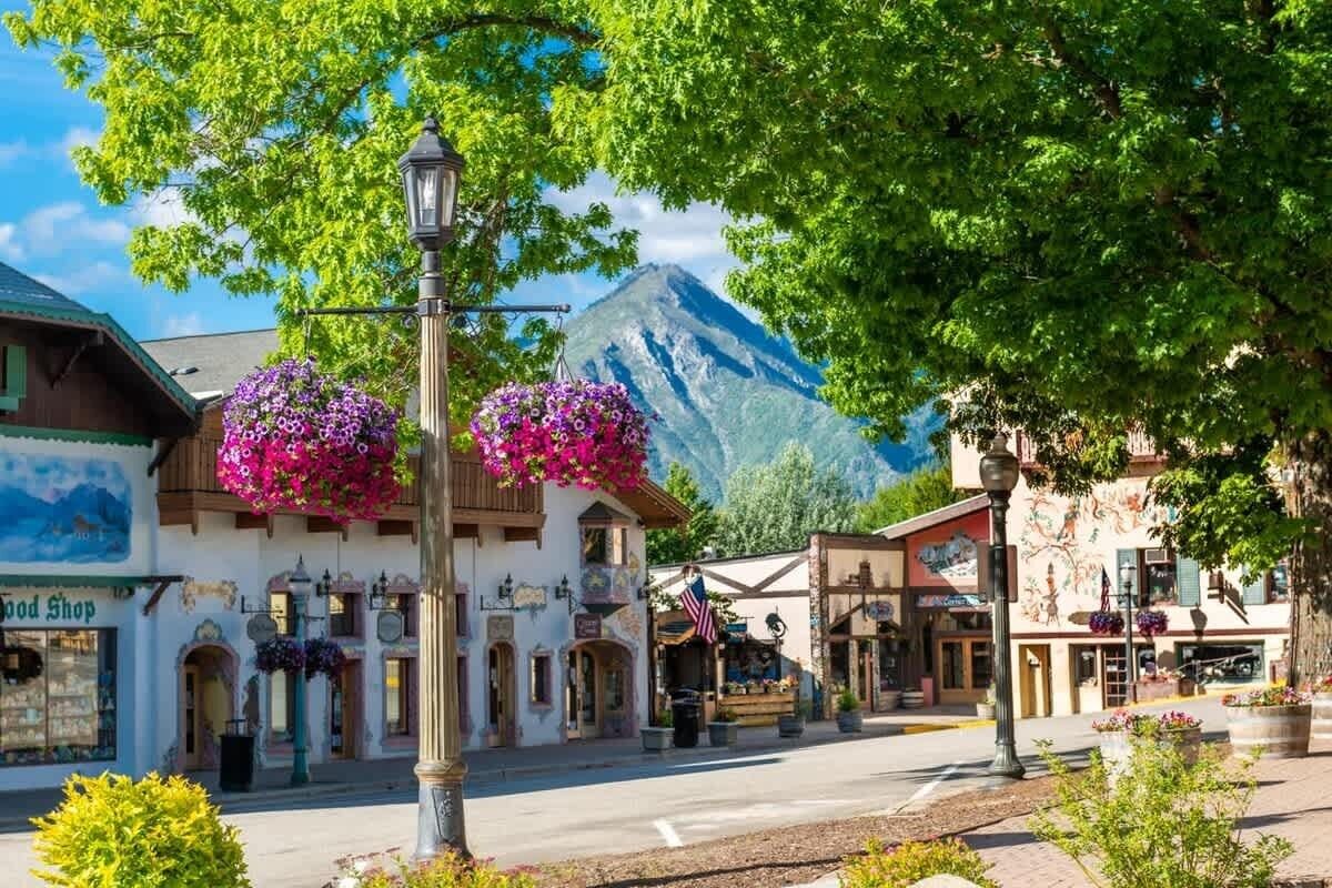 Una plaza de pueblo con edificios, un farol y cestas de flores colgantes.