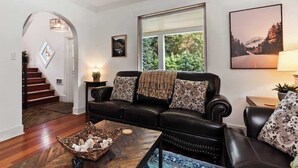 A living room with a black leather sofa, a wooden coffee table, and a large window with a view of greenery.