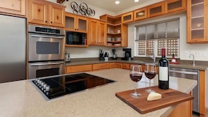 Una cucina moderna con mobili in legno, elettrodomestici in acciaio inossidabile e un'isola centrale con bicchieri da vino e una bottiglia.