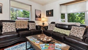 A cozy living room with two black leather sofas, a wooden coffee table with magazines, and a lamp on a side table.