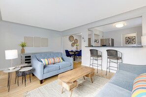 A modern living room with a blue sofa, a wooden coffee table, and a dining area with chairs and a table. - Spacious modern & central 3 bed/2 bath • Renovated • Garage • W/D • Pet-Friendly (St. Louis Park)