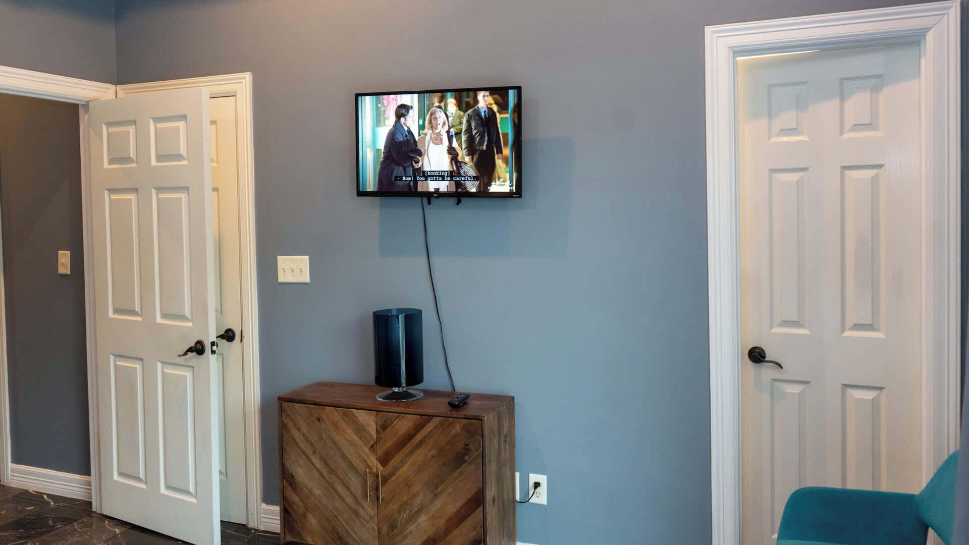 Un couloir avec un téléviseur fixé au mur, un meuble en bois avec une télécommande, et deux portes fermées.