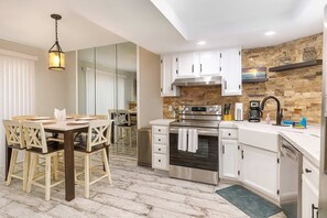 A modern kitchen with white cabinets, stainless steel appliances, and a brick accent wall. - Sweeping 5th Floor Views " Direct Beach " Remodele (South Padre Island)