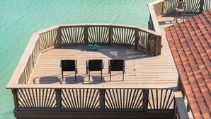 A wooden deck with a railing, three chairs, and a pair of blue shoes on the deck.