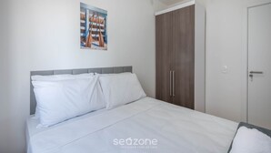 A bedroom with a bed, white bedding, a grey headboard, a wooden wardrobe, and a door. - Apart w/ BBC 750 m From the Beach Sfr0411 (Barra Velha)